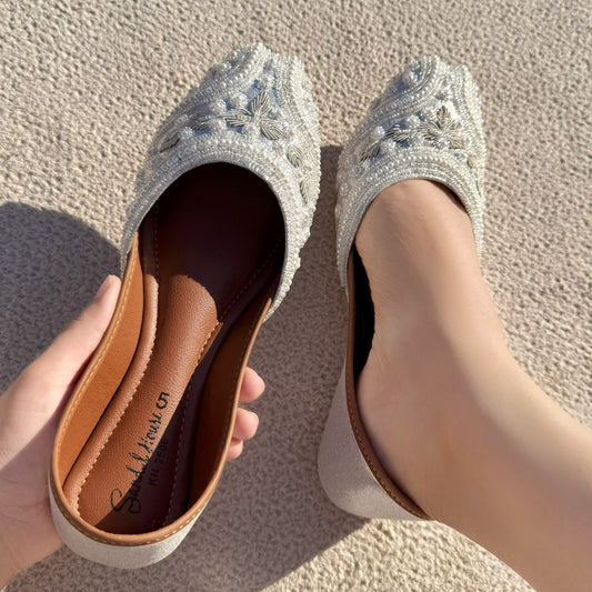 Silver embellished shoes with a brown insole held by a hand on a textured surface.